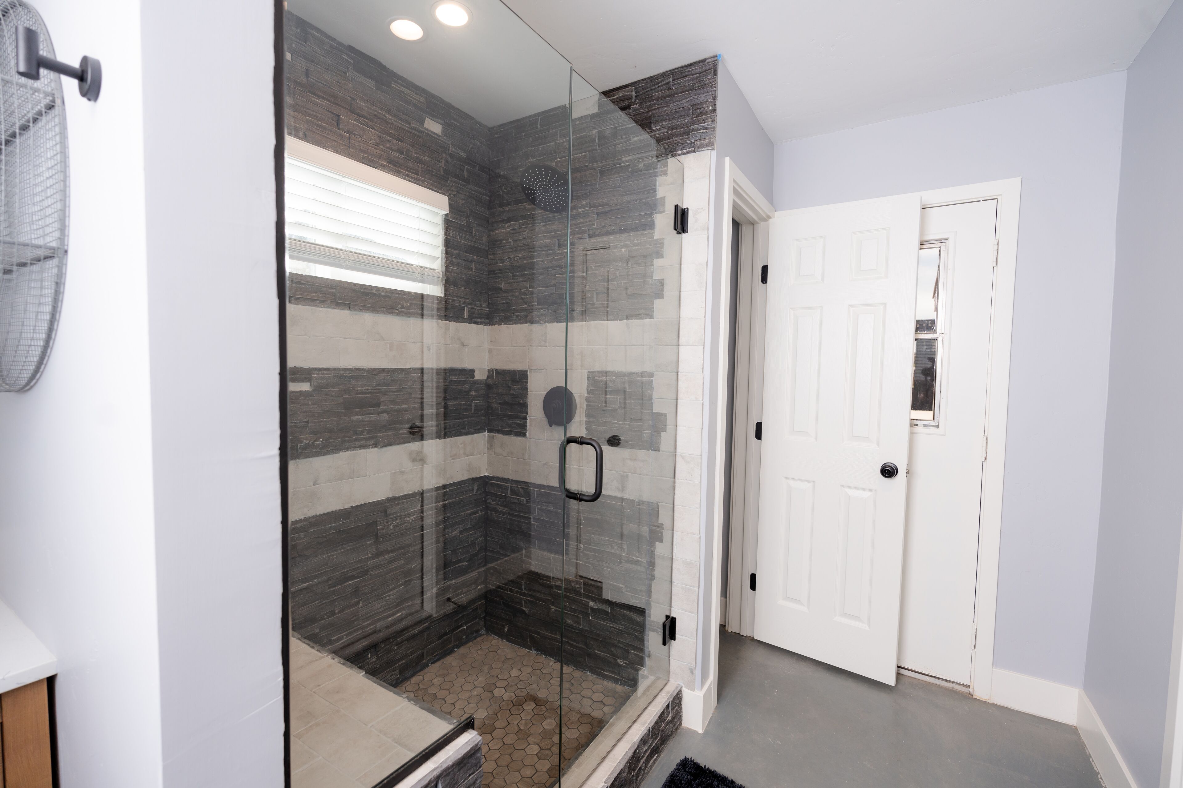 A modern bathroom with a glass-enclosed shower, tiled walls, and a white door.