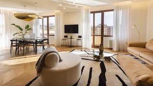 A modern living room with a round coffee table, a sofa, a dining area with a table and chairs, and a TV mounted on the wall. - Oro1 Florence Luxury Apartment by Mmega (Florence)