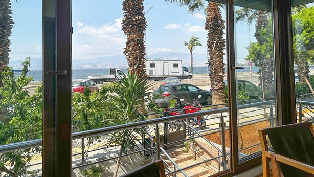 A balcony with a view of a busy street, palm trees, and a body of water. - The Next Suites (Izmir)