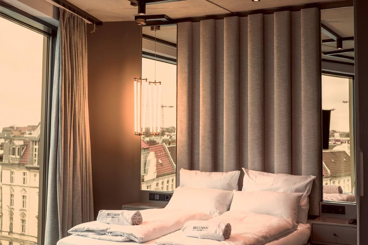 A modern bedroom with a large bed, a view of the city, and a cityscape visible through the window.