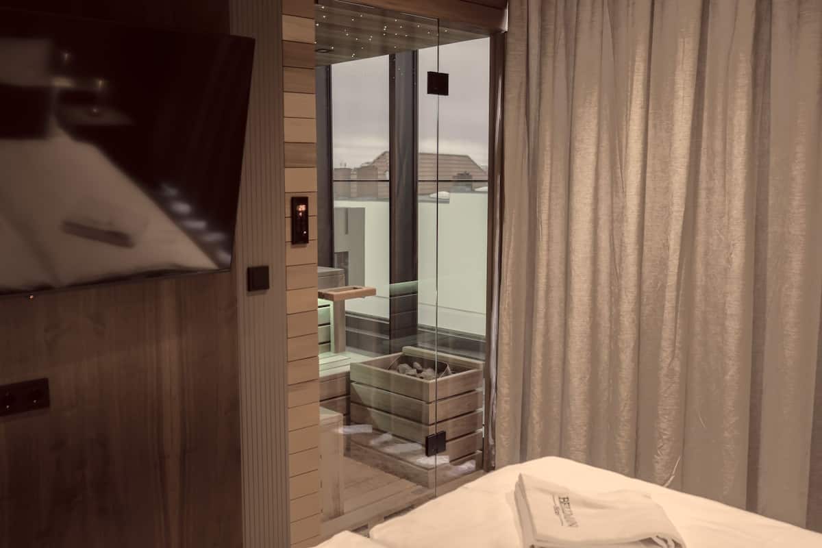 A modern hotel room with a sliding door leading to a balcony, a bed with a neatly made white bedspread, and a wooden wall paneling.
