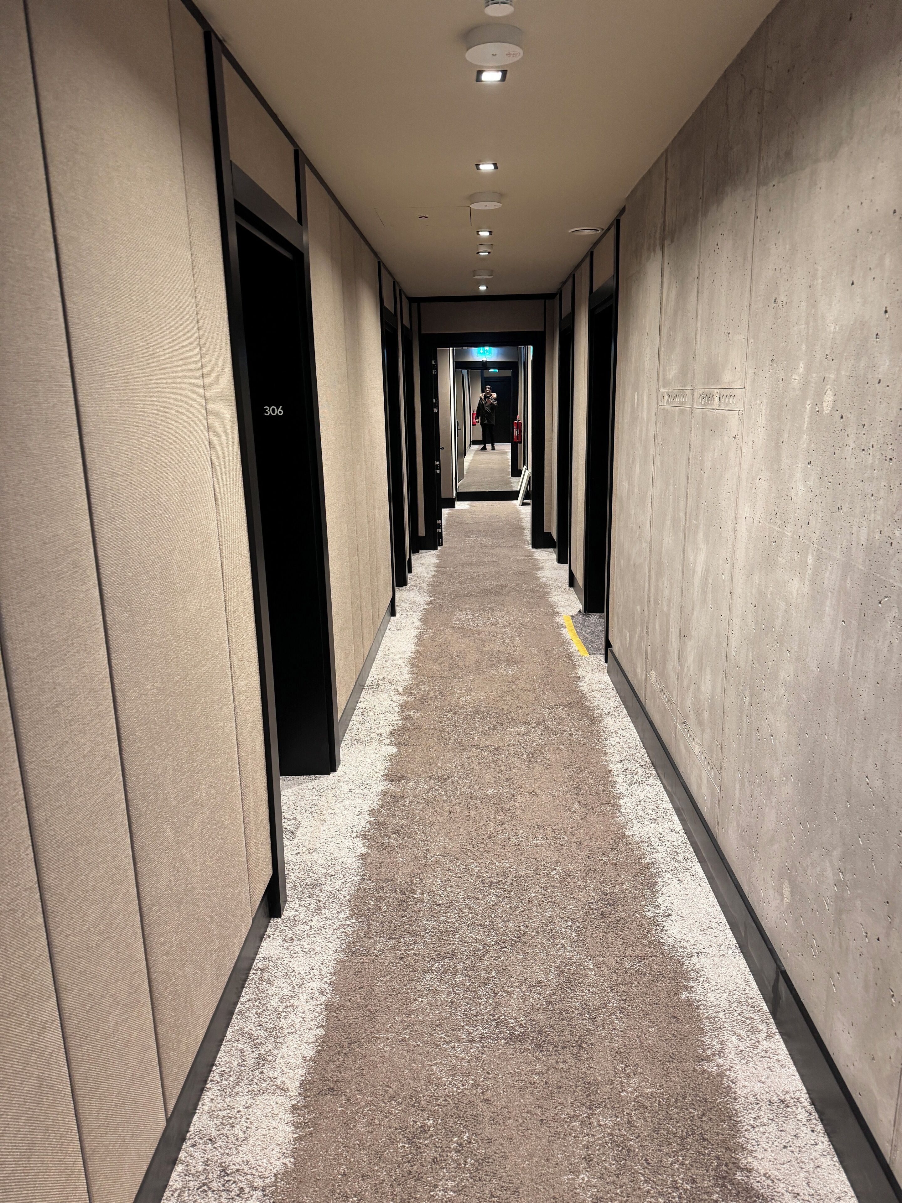 Un long couloir étroit, avec des portes de chaque côté, un sol recouvert de moquette et un plafond doté d’un éclairage encastré.