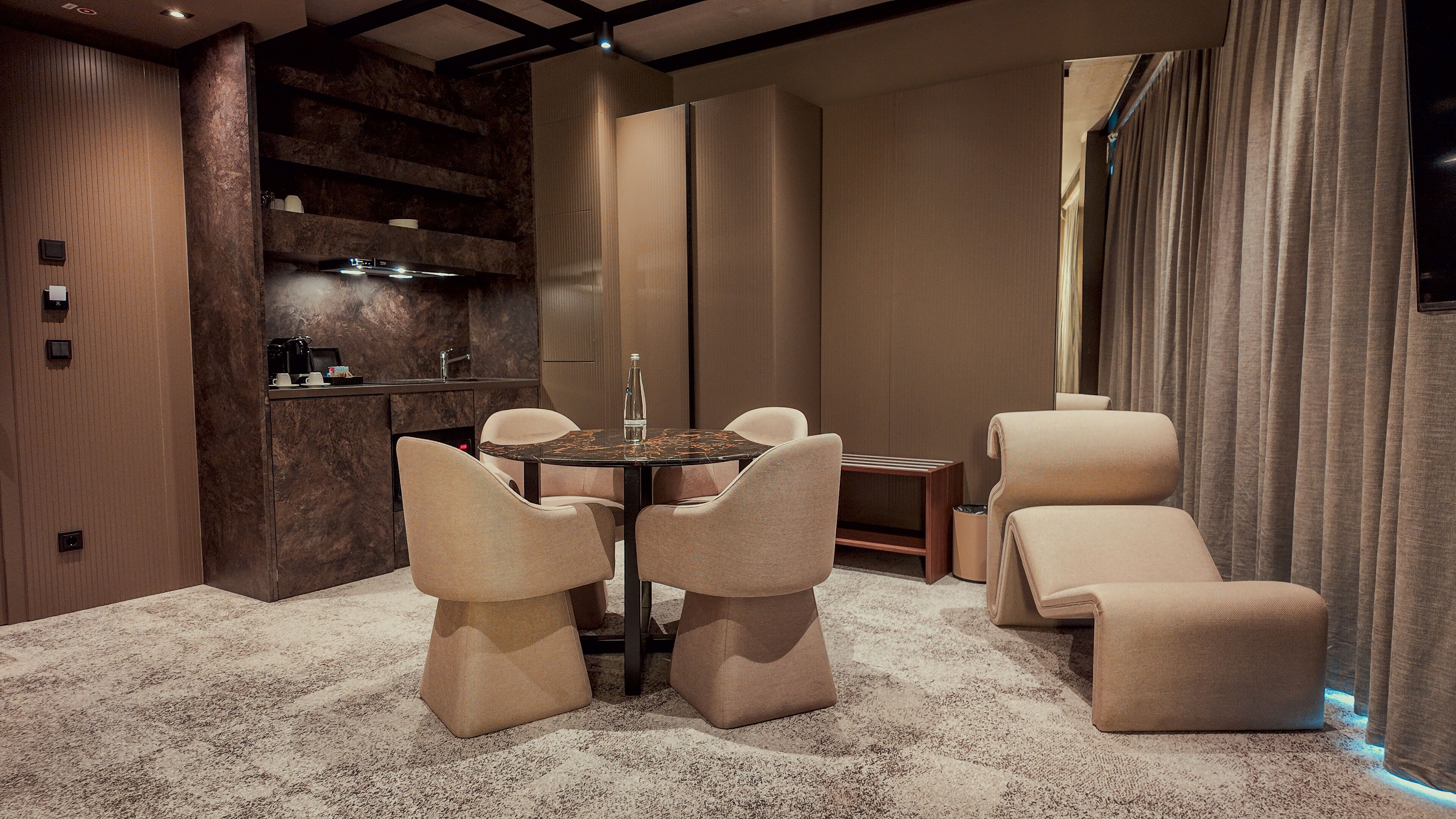 A modern dining area with a marble table, cushioned chairs, and a built-in kitchen with a sink and countertop.