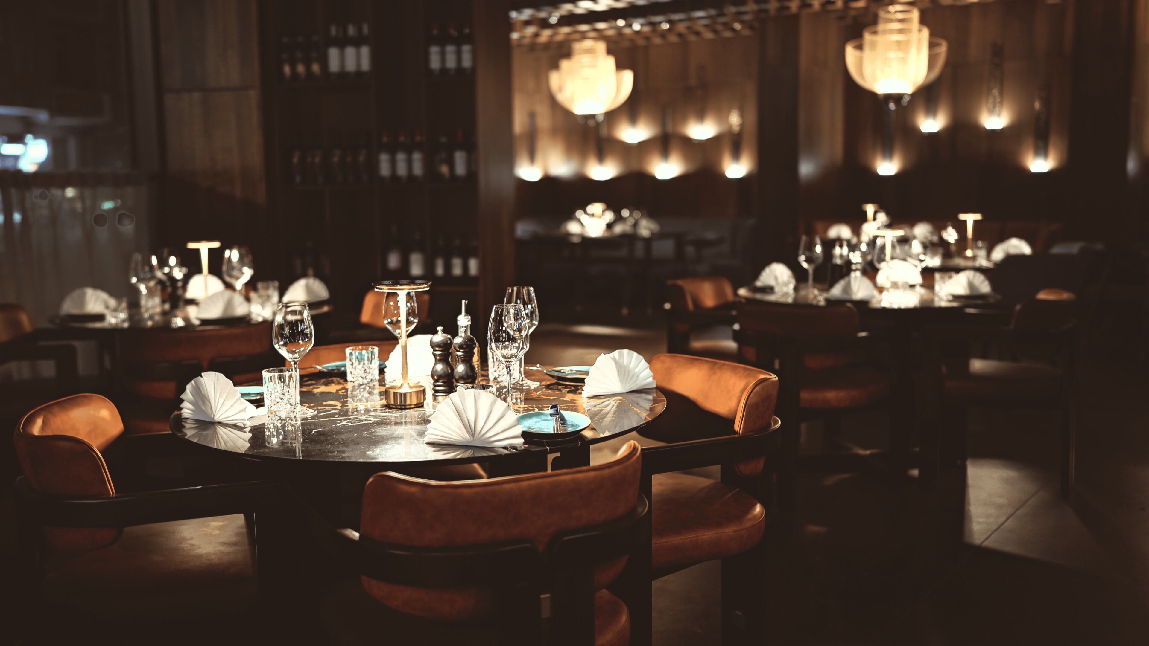 Een restaurant met gedimd licht, rondedienen tafels en lederen stoelen, met een warme sfeer.