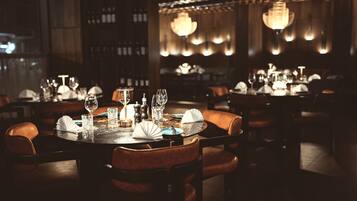 Een restaurant met gedimd licht, rondedienen tafels en lederen stoelen, met een warme sfeer.