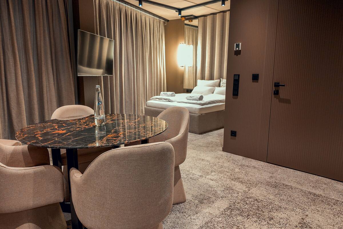 A hotel room with a round table, two chairs, a bed, and a wardrobe.