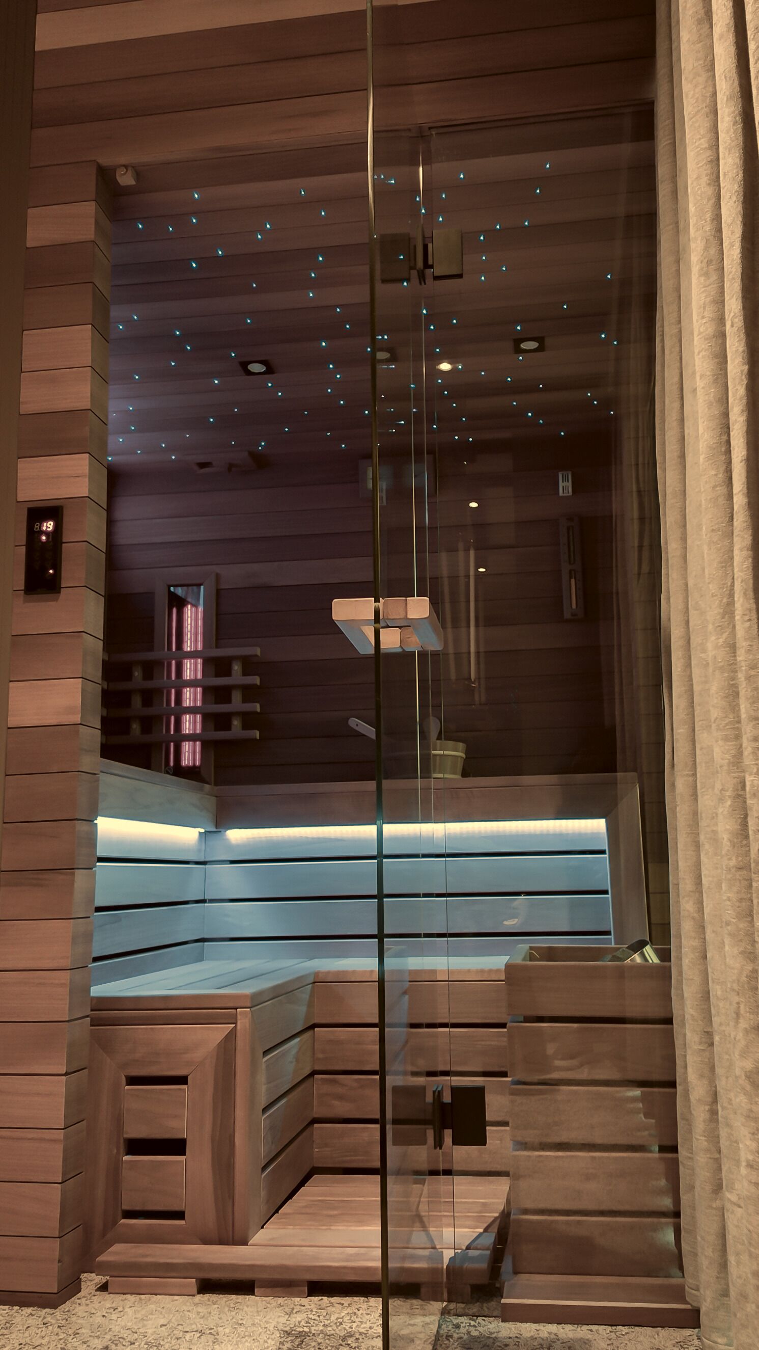 A modern spa room with a glass partition, wooden benches, and a ceiling with small lights.