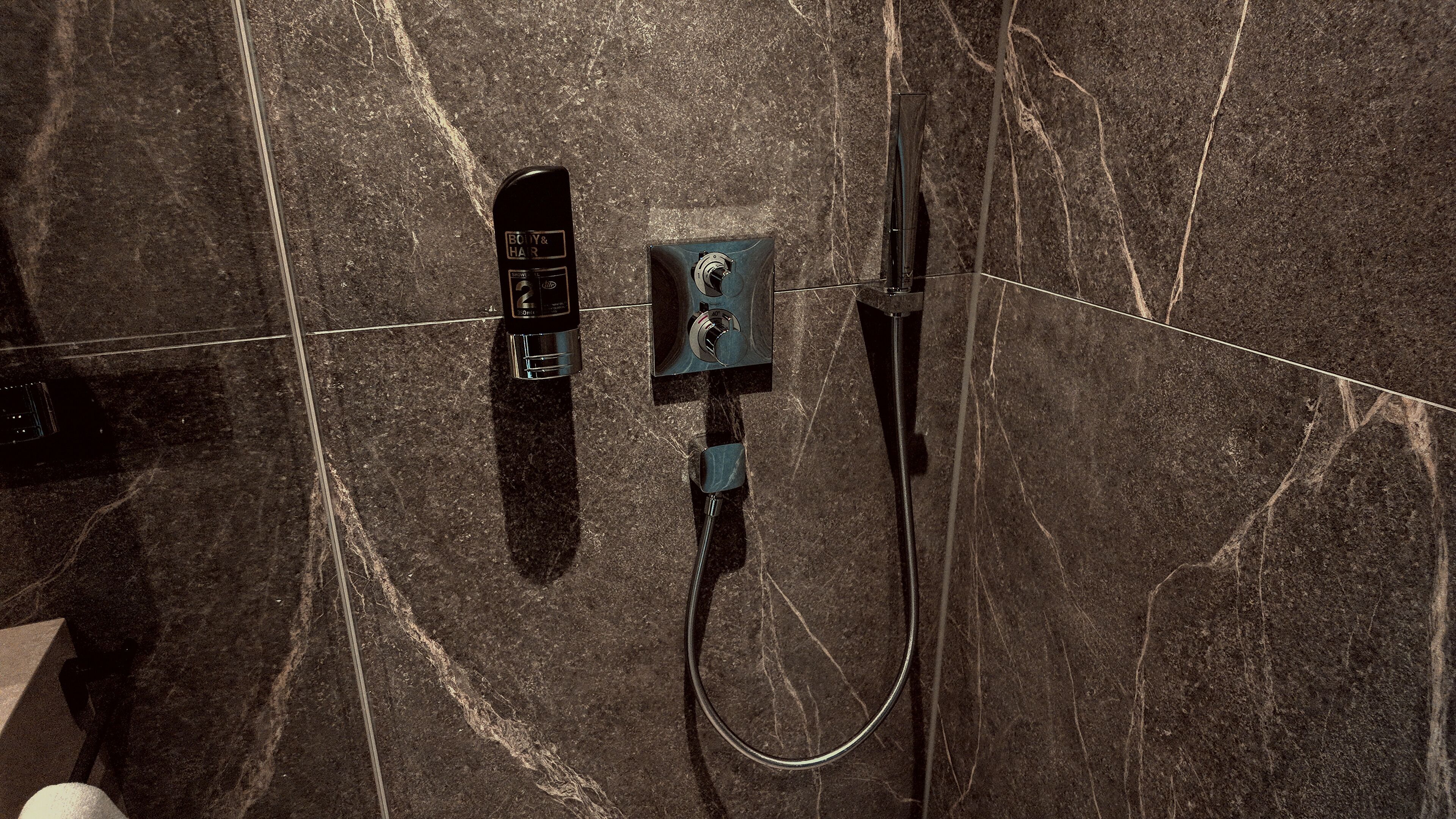 Un baño con un cabezal de ducha manual negro, un panel de control en la pared y un grifo de pie.