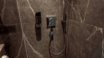 Un baño con un cabezal de ducha manual negro, un panel de control en la pared y un grifo de pie.