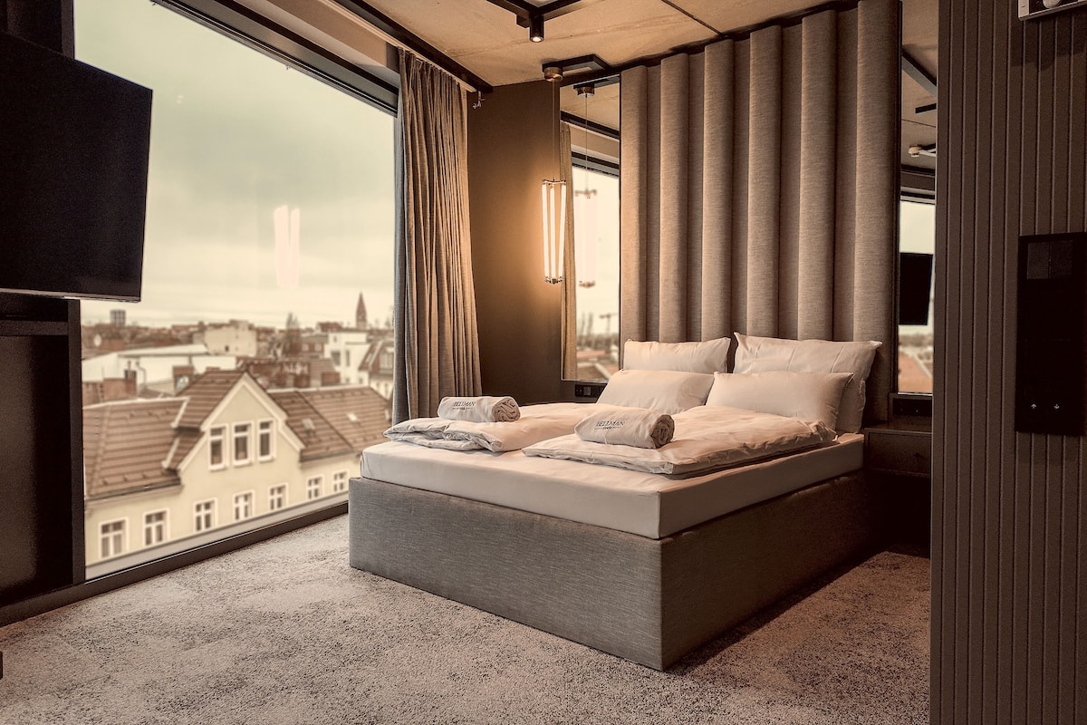 A modern bedroom with a large bed, a view of the city, and a flat-screen TV.