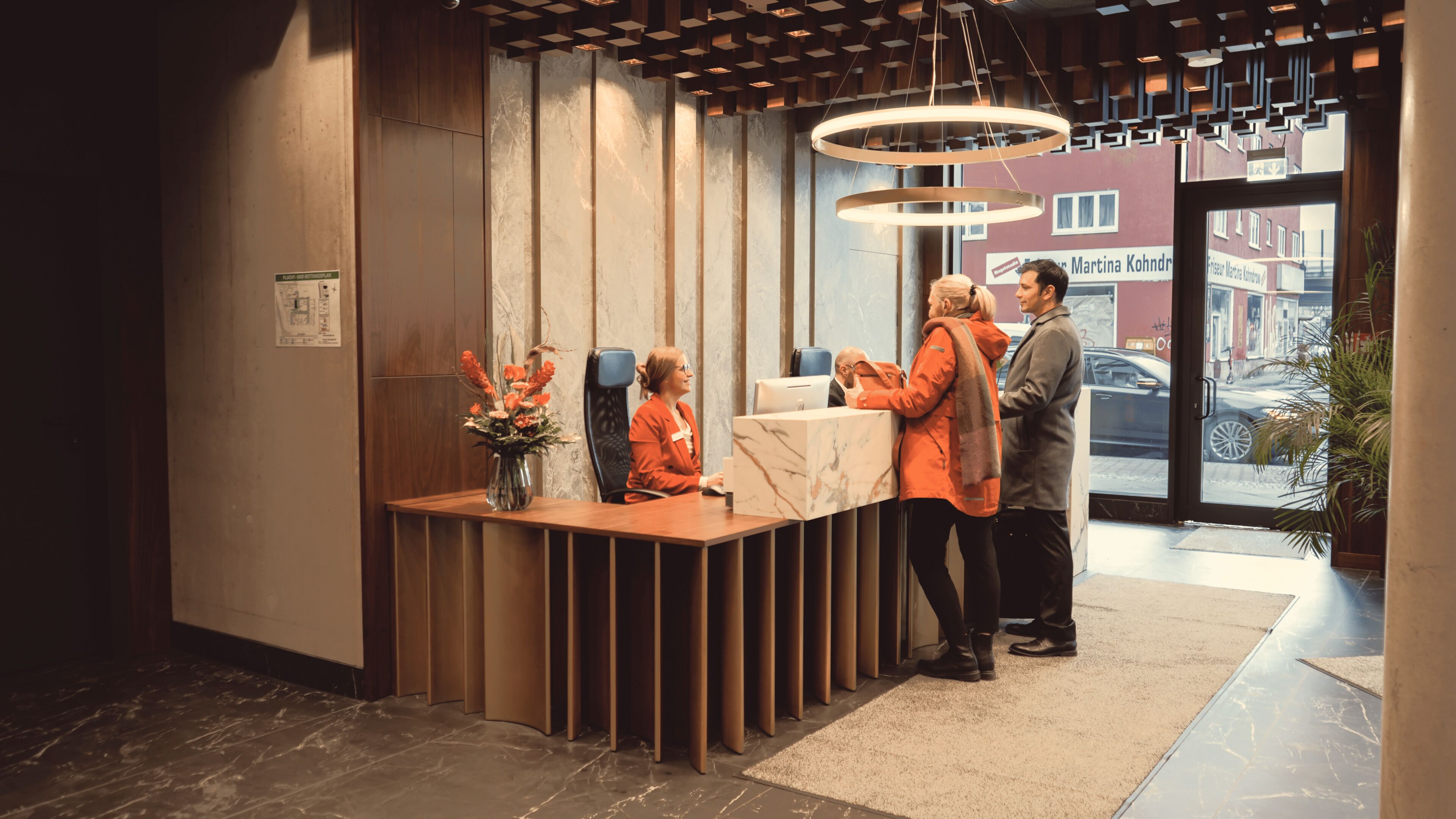A reception desk with a vase of flowers, a modern interior with wooden paneling, and a view of the street outside.