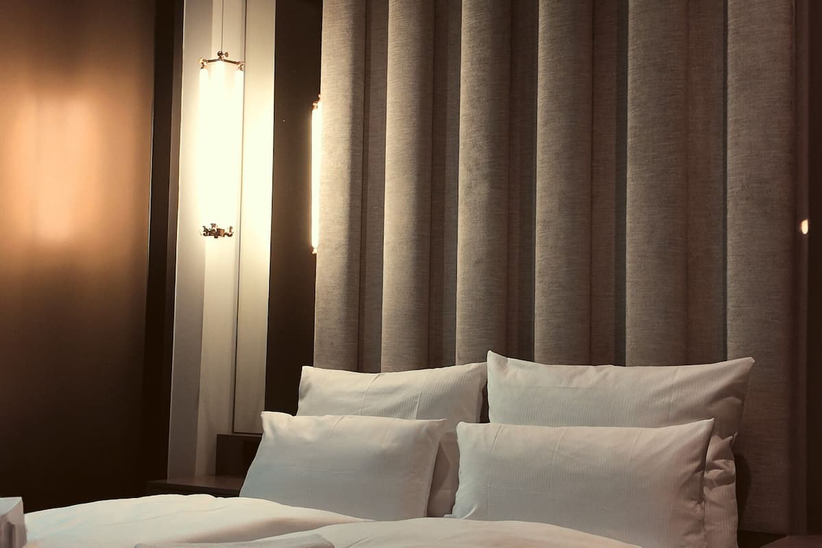 A hotel room with a large bed, a nightstand, and a wall-mounted light fixture.