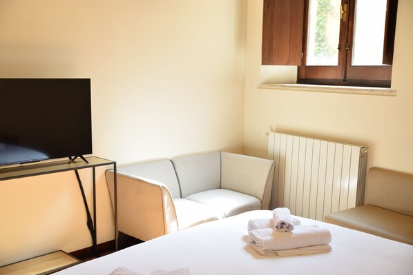 Habitación de hotel con cama, televisión sobre un mueble, sofá y ventana con vista a zonas verdes.