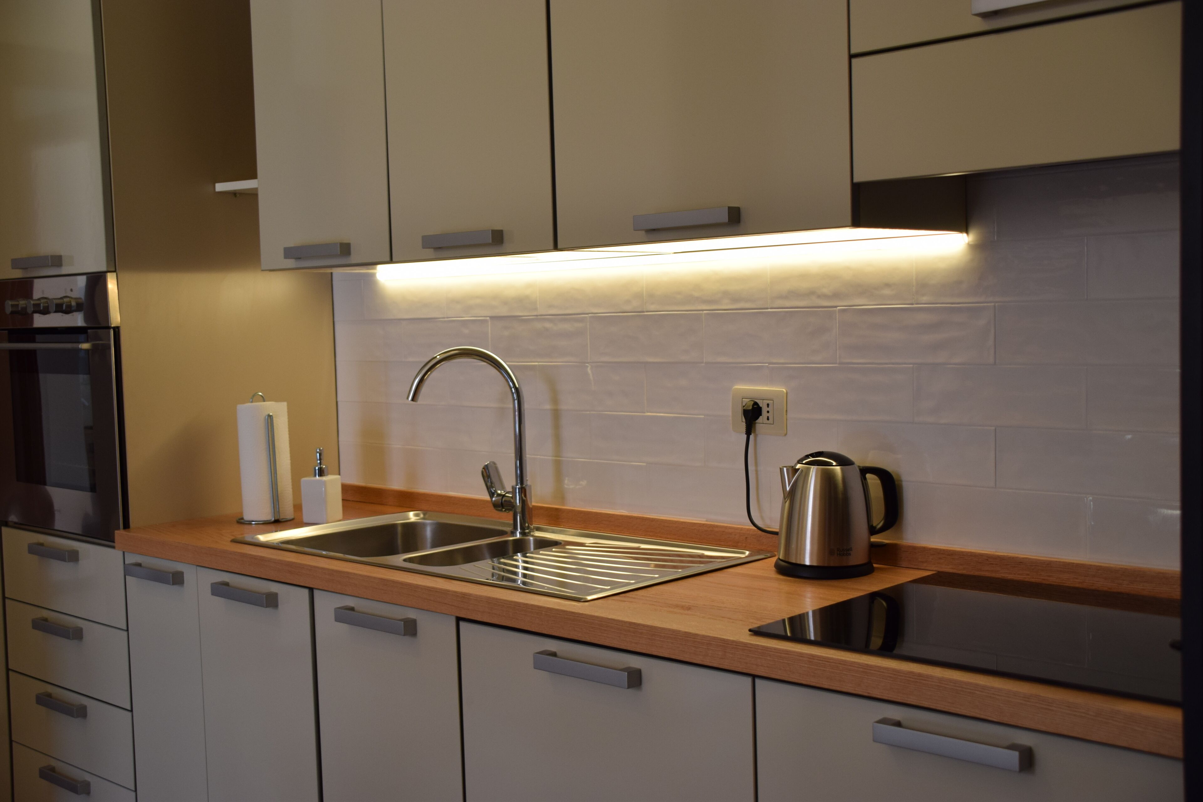 Una cocina moderna con un lavamanos de acero inoxidable, una tetera y un horno empotrado.