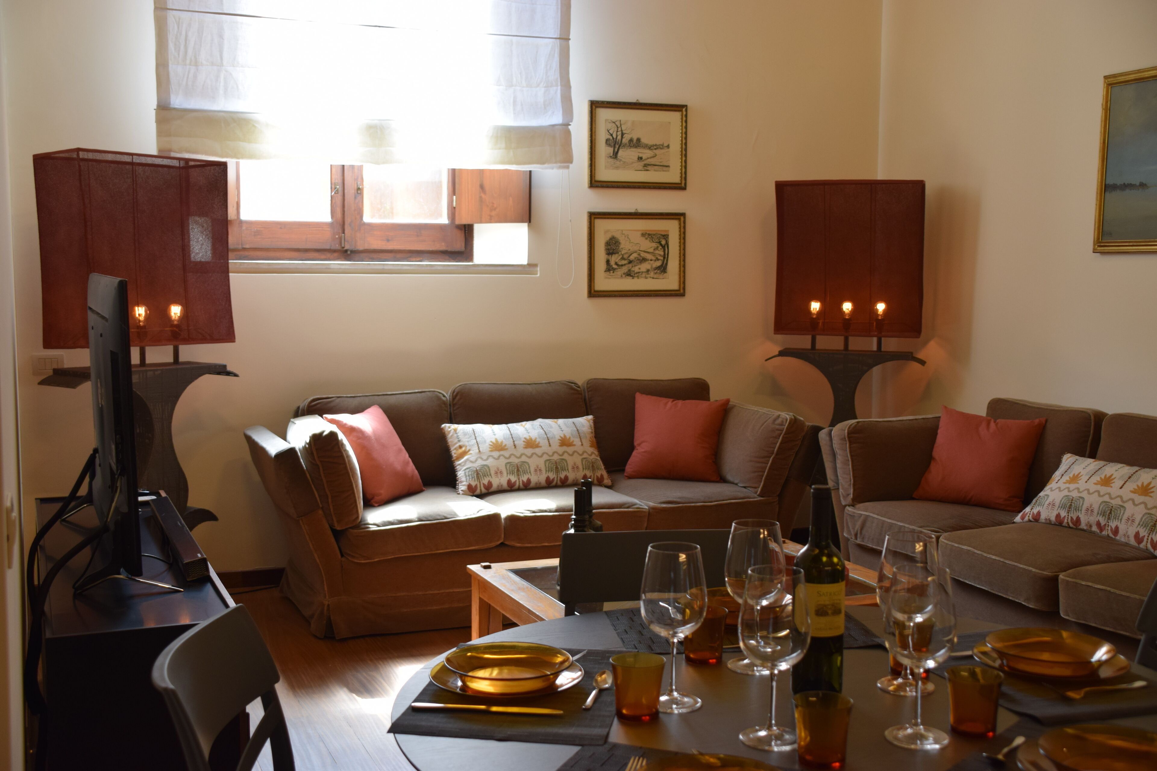 A cozy living room with a brown sofa set, a dining table set for four, and a television on a stand.