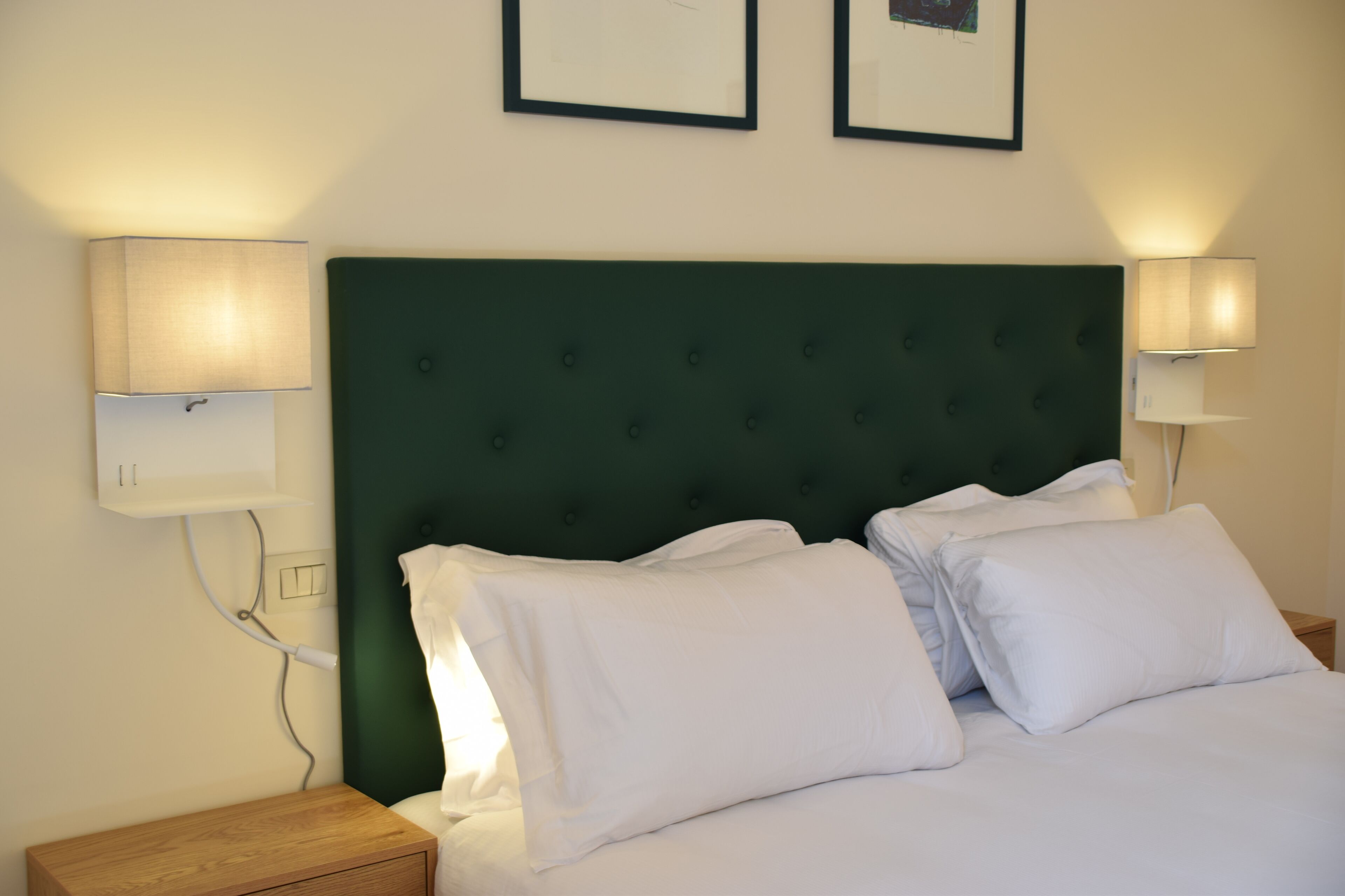 A neatly made bed with white linens, a green upholstered headboard, and two bedside lamps on either side.