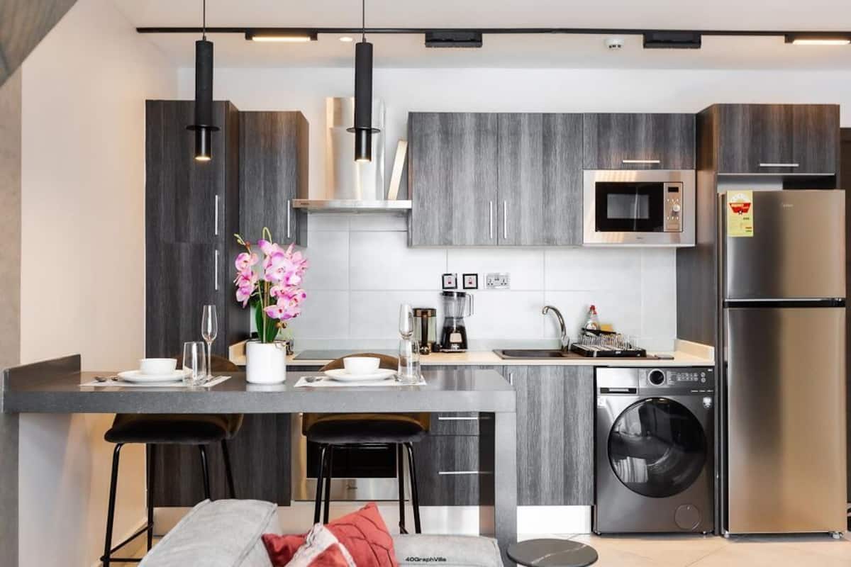 A modern kitchen with grey cabinetry, a built-in microwave, a stainless steel refrigerator, and a washing machine.