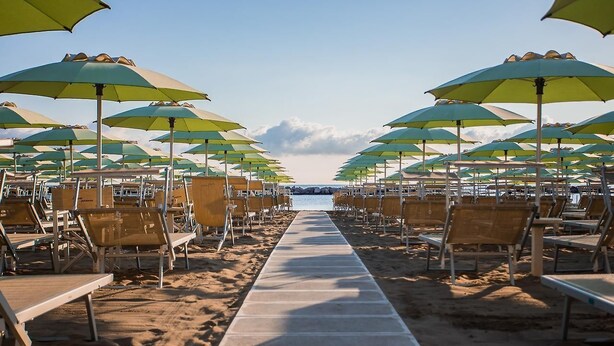 Une plage bordée de rangées de transats et de parasols, une promenade en béton et une vue sur la mer.