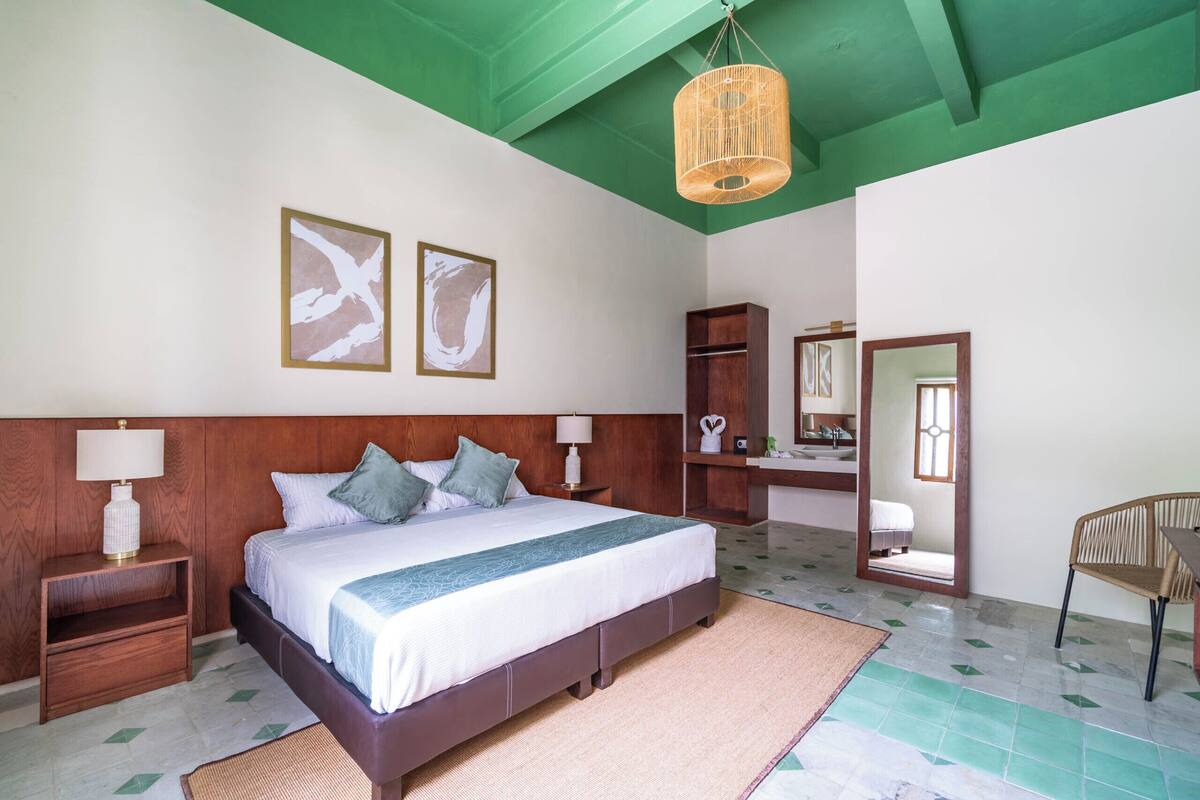 A bedroom with a large bed, wooden headboard, bedside tables with lamps, a mirror, and a chair.