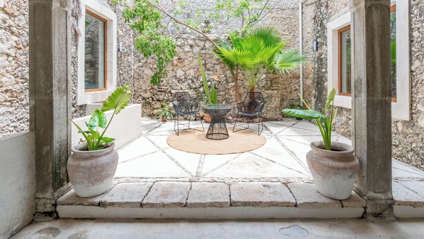 A courtyard with a stone wall, a round table with chairs, and potted plants. - Hotel Boutique Santa Elena (Mérida)