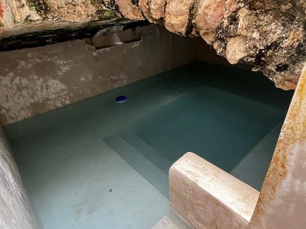 A stone-walled room with a small pool and a blue object on the floor.