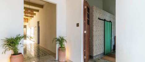 A hallway with a tiled floor, two potted plants, and a door with a green handle.