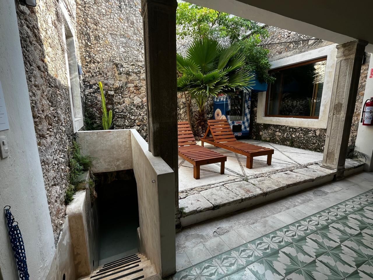Un espacio exterior cubierto con pared de piedra, banco de madera y suelo de baldosas.