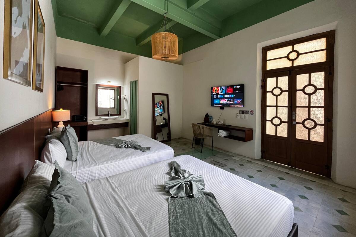 A hotel room with two beds, a desk, a TV, and a large window with a decorative door.