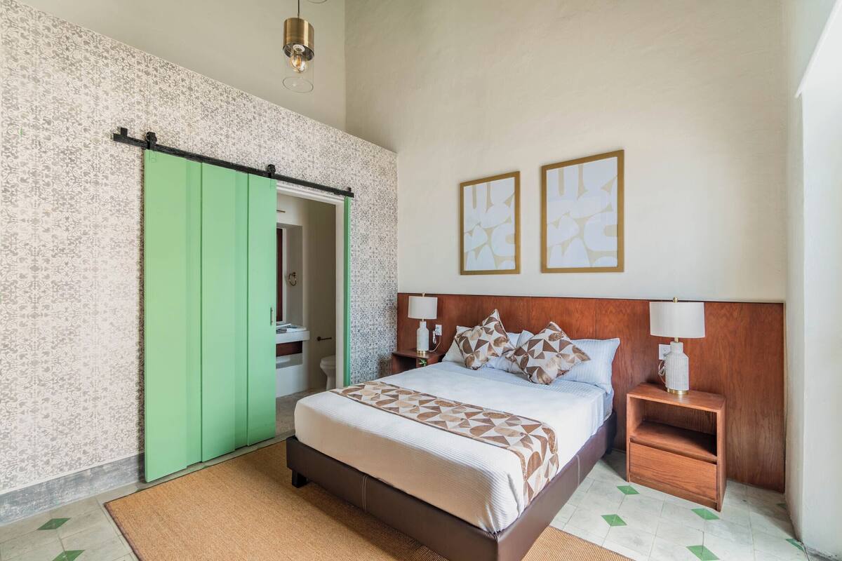 A bedroom with a bed, nightstands, a green wardrobe, and two framed pictures on the wall.