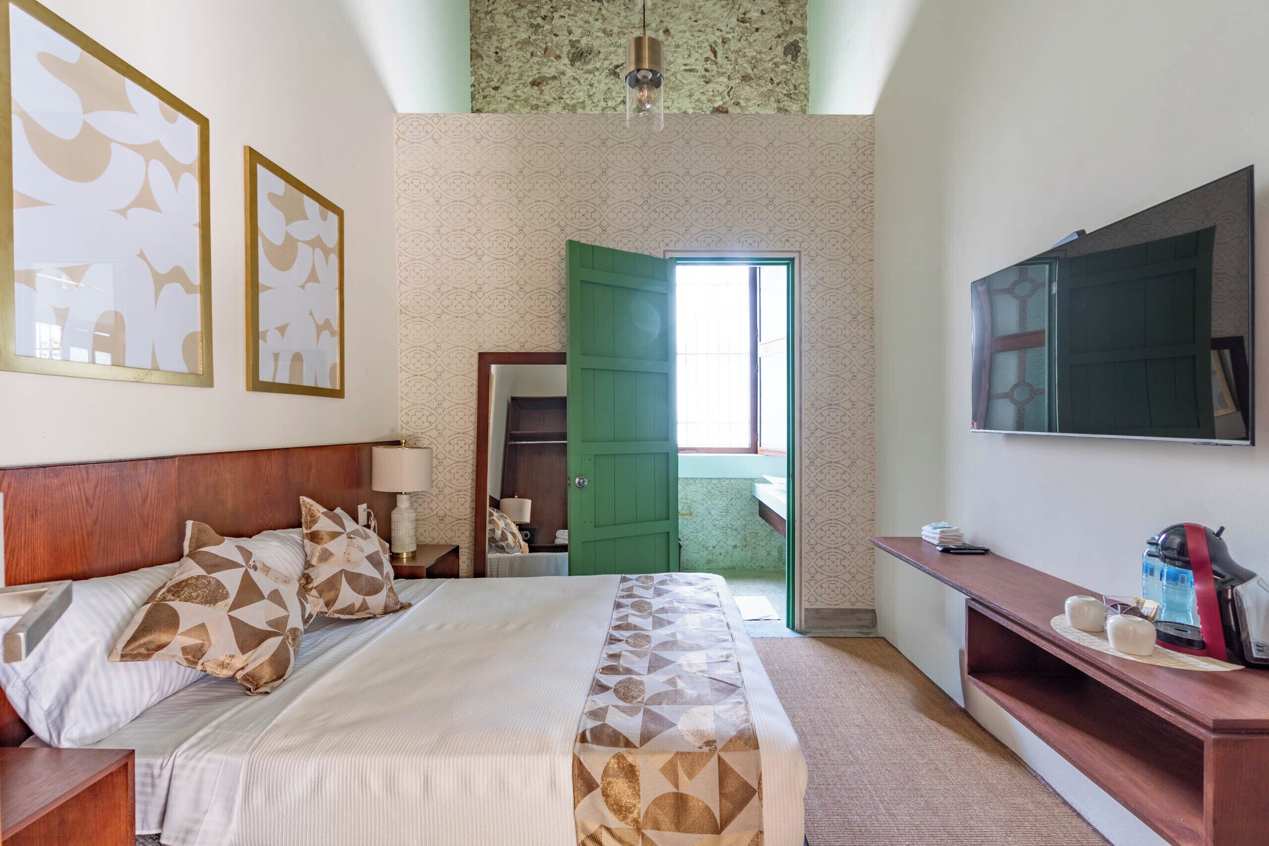 A hotel room with a bed, bedside tables, a TV, a green door, and a view of the outside.