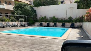 Ein rechteckiger Pool mit Holzterrasse, umgeben von Liegestühlen und Grünpflanzen.