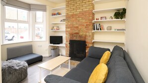 A living room with a brick fireplace, grey sofa, and white shelves with books and decorative items. - ☀ Sunny, Victorian 2BR Townhouse ☀ Oxford - Pass the Keys (Oxford)