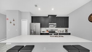 A modern kitchen with dark cabinets, a white countertop, and stainless steel appliances. There are two bar stools in front of the counter. - EV_1569 - 4 Bed 3 Bath Townhome with Screened-In Splash Pool, Kids Room (Davenport)