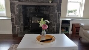 A living room with a stone fireplace, a flat-screen TV mounted above it, a white coffee table with a vase of flowers, and a beige sofa.