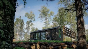 Een moderne cabin met een glazen gevel, omgeven door een natuurlandschap met grote rotsen en bomen.