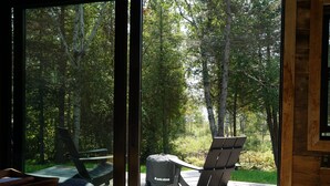 Een terras met twee Adirondack-stoelen, een solo kachel en uitzicht op een bos.