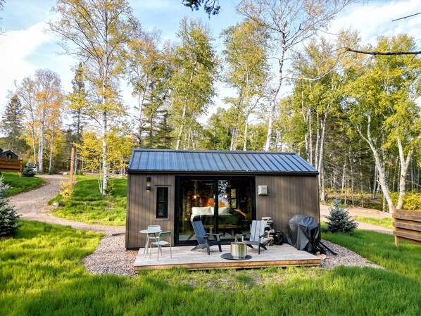 A small cabin with a deck, outdoor seating, and a fire pit.