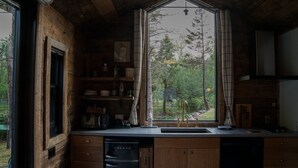 A kitchen with wooden cabinets, a built-in dishwasher, and a window with a view of trees.