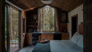 A bedroom with a large bed, wooden cabinets, a built-in desk, and a window overlooking a forest.