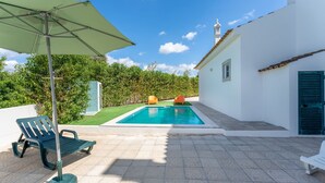 Ein Swimmingpool mit zwei orangefarbenen Stühlen, einem grünen Sonnenschirm und einer Sitzbank.