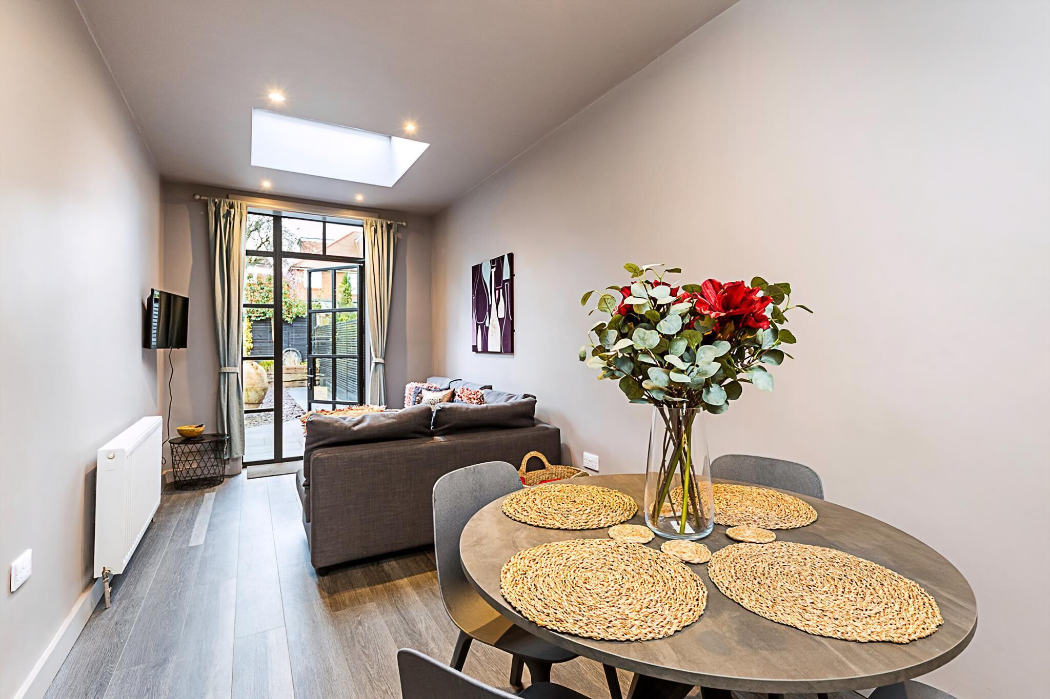 A modern living room with a dining area, a sofa, a TV, and a large window with curtains.