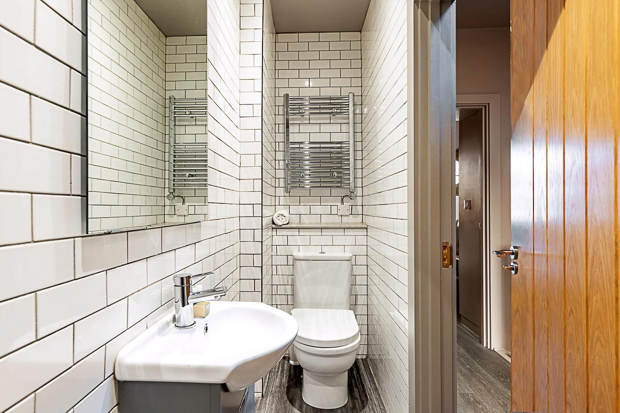 A modern bathroom with white tiled walls, a white sink, and a toilet.