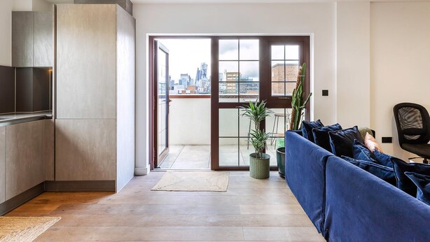 A modern living room with a city view, a sofa, a chair, and a kitchen area. - City View Spacious 2 Bedroom Penthouse (London)