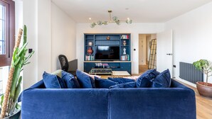 A living room with a blue sofa, a television, and a bookshelf. - City View Spacious 2 Bedroom Penthouse (London)