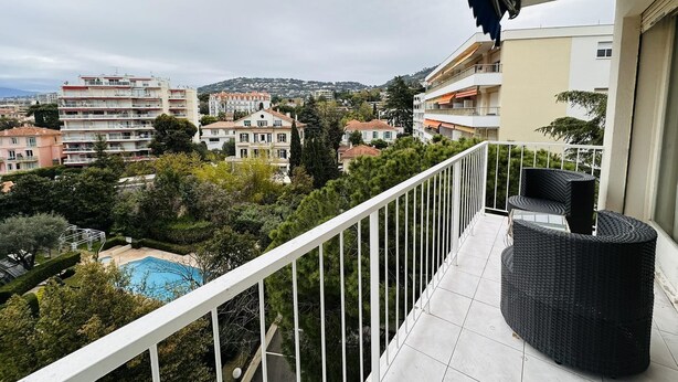 A balcony with a view of a swimming pool, surrounding buildings, and a hilly landscape.