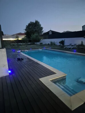 A swimming pool with a wooden deck and blue ambient lighting.