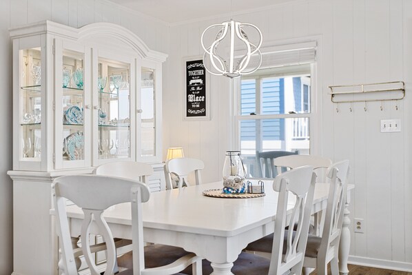 A dining room with a white table, white chairs, and a glass cabinet with decorative items.