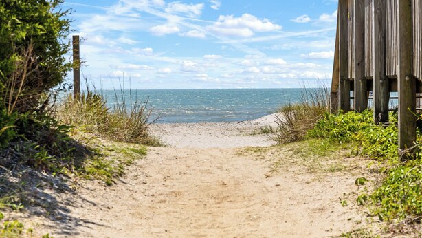 Ein Sandweg am Strand, der zum Meer führt, mit einer Holzkonstruktion auf der rechten Seite.