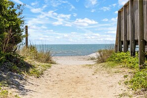 A sandy beach path leading to the sea with a wooden structure on the right.