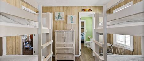 A bunk room with wooden walls, a dresser, and a view into another room.